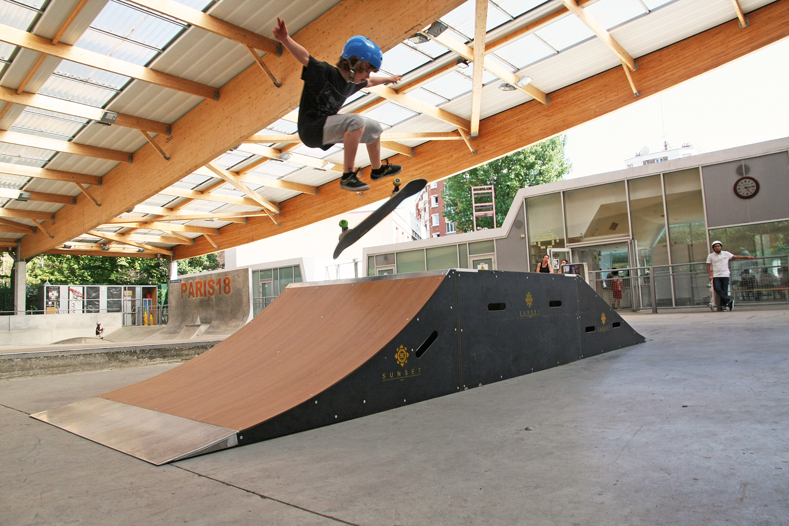 Enfant casqué effectuant un trick de skateboard sur une rampe dans un skatepark couvert