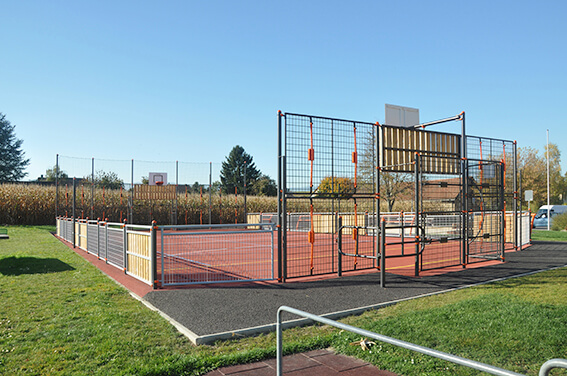 Un terrain de sport multifonctionnel clôturé avec des paniers de basket-ball et des buts de football, entouré d'espaces verts.