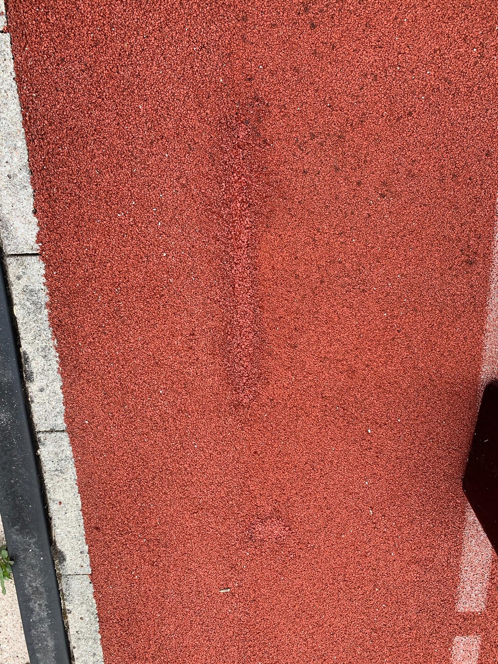 Rote Laufbahnoberfläche mit Teer und Randstein