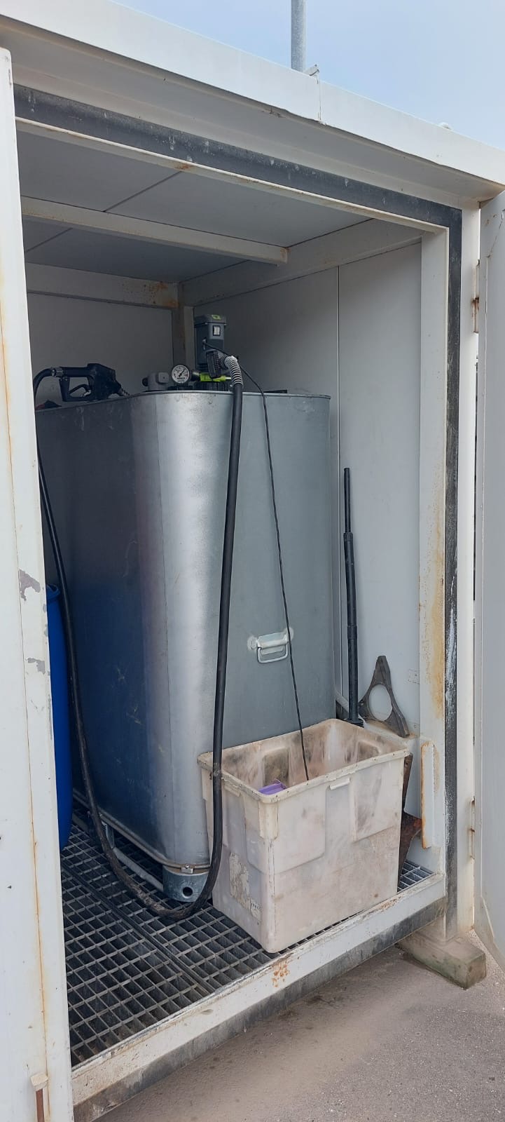 Großer metallischer Tank mit Schläuchen und Zubehör in einem weißen Lagercontainer