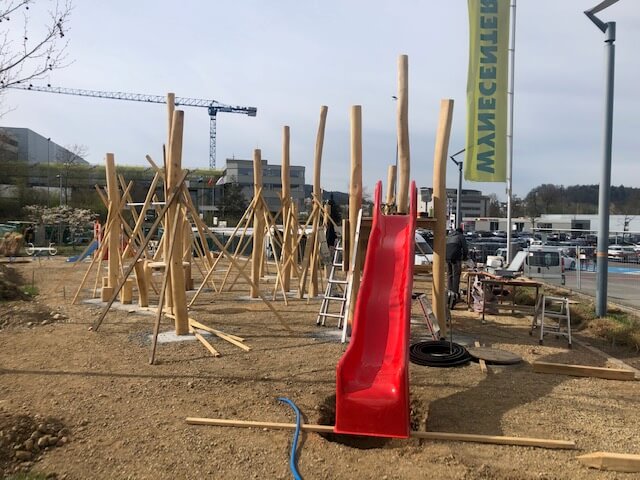 Eine Baustelle für einen Spielplatz mit einer roten Rutsche und Holzstrukturen.
