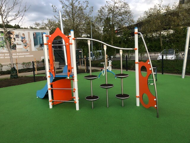 Ein moderner Spielplatz mit einem bunten Klettergerüst aus Metall und Kunststoff, umgeben von grünem Kunstrasen.