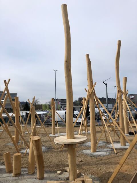 Une nouvelle aire de jeux avec de hautes structures en bois en construction, entourée d'un décor urbain.