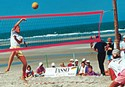 Des joueurs en train de jouer au beach-Volleyball, un ballon jaune en l'air, des spectateurs sur la plage, la mer en arrière-plan