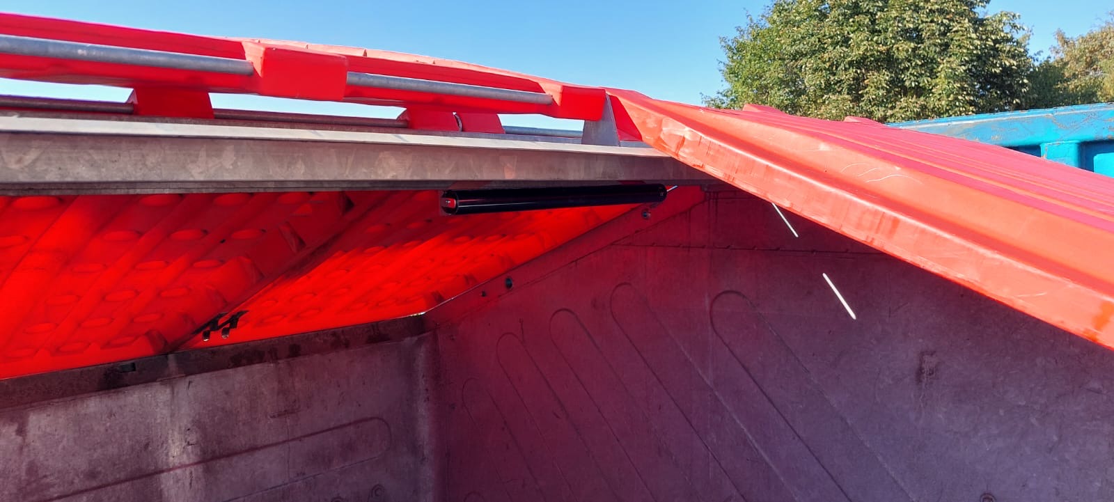 Innenansicht eines offenen Müllcontainers mit rotem Deckel, Metallverstärkung und klar sichtbarem Himmel im Hintergrund