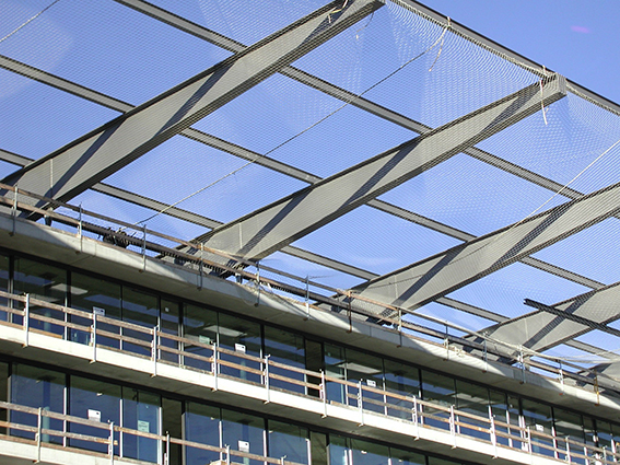 Detailansicht eines modernen Bürogebäudes mit Glasfassade und einem ausgefallenen architektonischen Sonnenschutz aus Metallstreben und Netz.