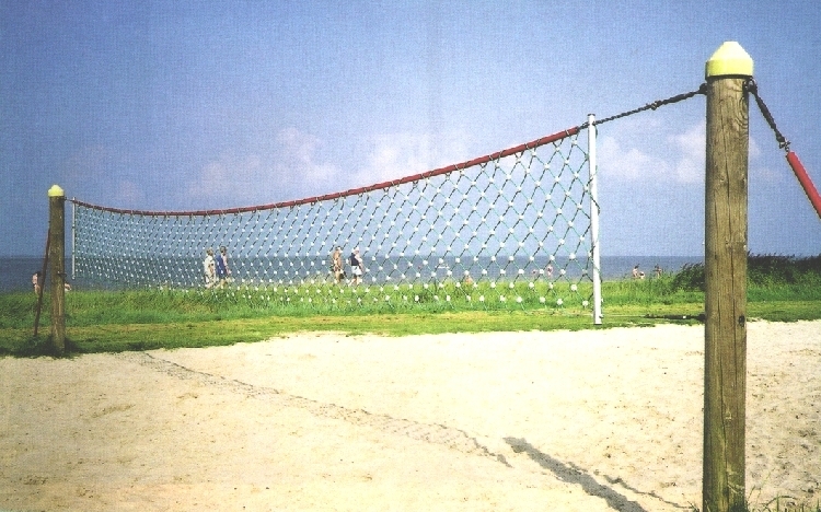 Volleyballnetz an einem Sandstrand mit Menschen im Hintergrund und Meerblick
