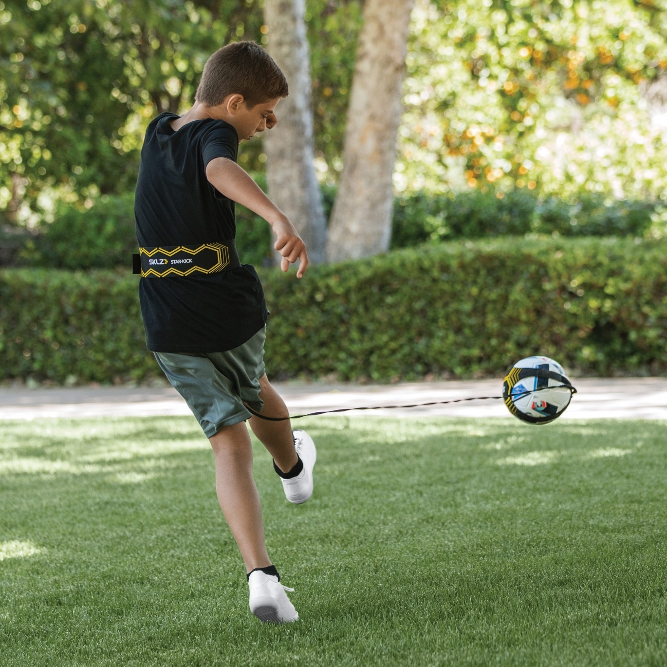 Un garçon joue dans le jardin avec un ballon de football attaché à un harnais d'entraînement.