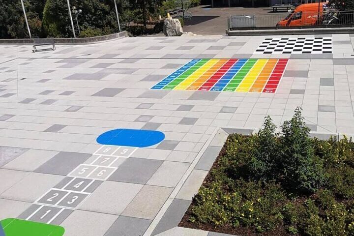 Une place pavée avec des aires de jeux colorées, dont un jeu classique de saut et un champ de chiffres.