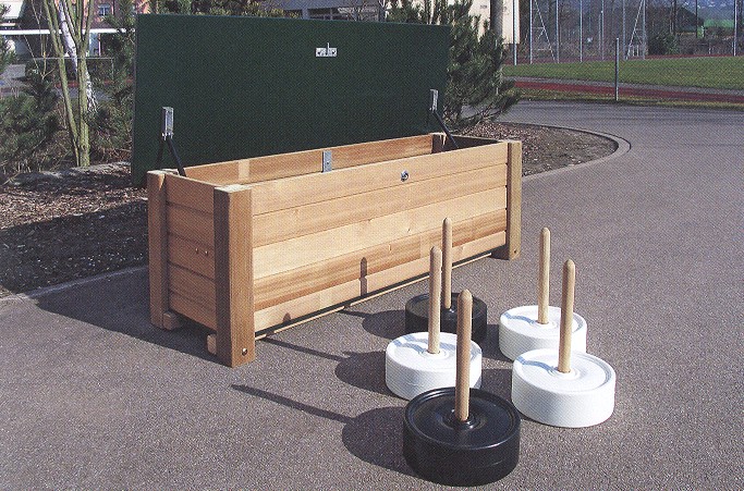 Abbildung eines Outdoor Spielgeräte-Sets bestehend aus einer großen Holzbox und mehreren Gewichtsplatten mit Holzstangen, auf einem Spielplatz aufgestellt.