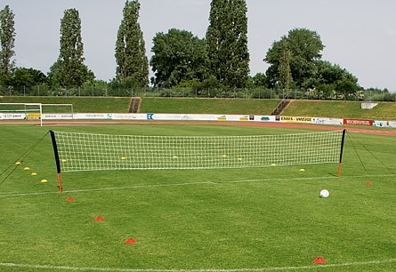 Un filet de sport mobile sur un terrain de football, entouré de cônes de marquage, avec des arbres en arrière-plan.