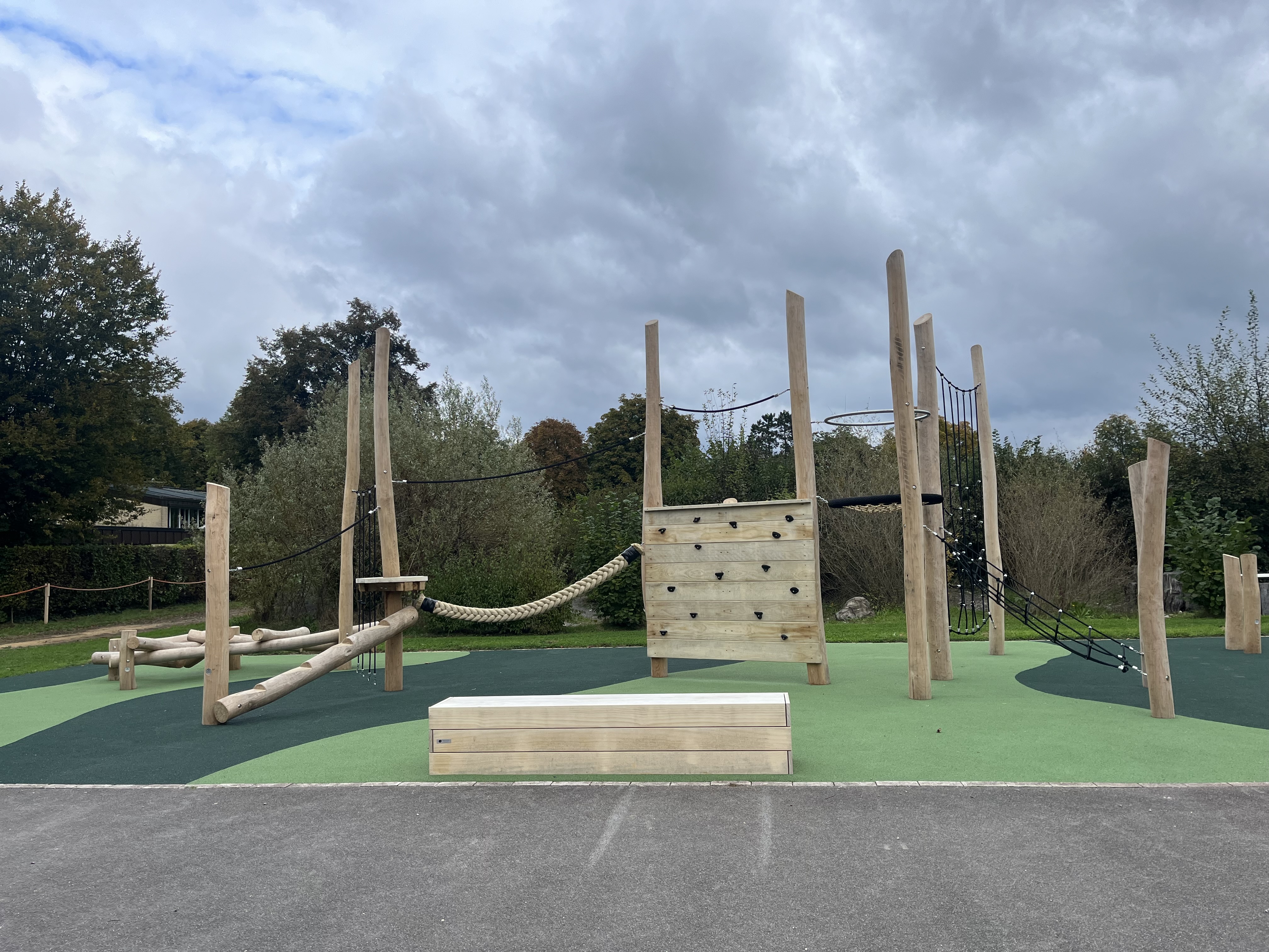 Moderner Spielplatz aus Holz mit verschiedenen Kletterelementen und Naturkulisse im Hintergrund