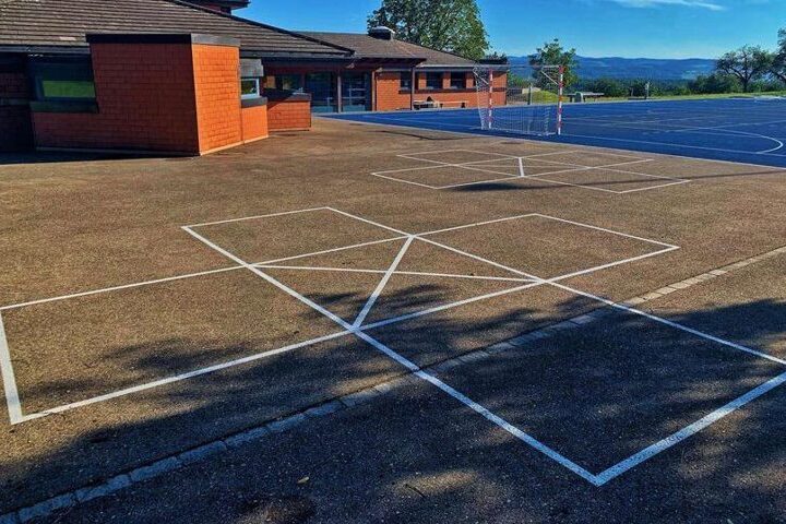 Une cour d'école vide avec des marquages au sol et un bâtiment en arrière-plan sous un ciel bleu
