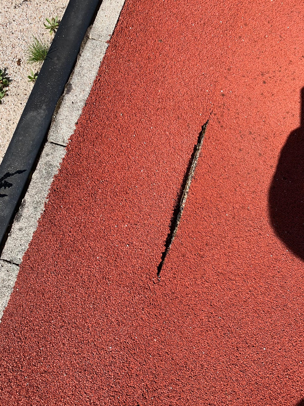 Ein Riss in einer roten Laufbahn nahe einem Pflasterrand.