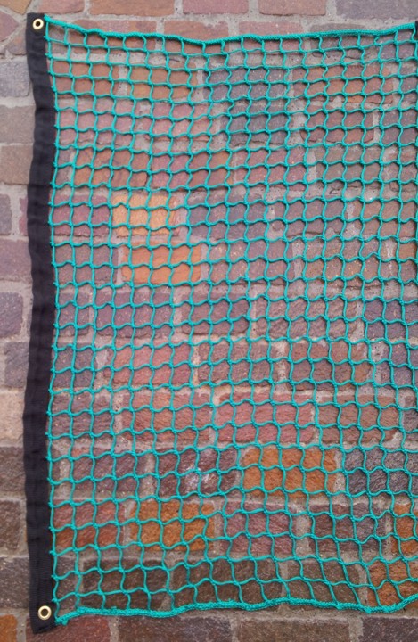 Ein grünes Sicherheitsnetz, das an einer Ziegelwand hängt und mit Ösen befestigt ist