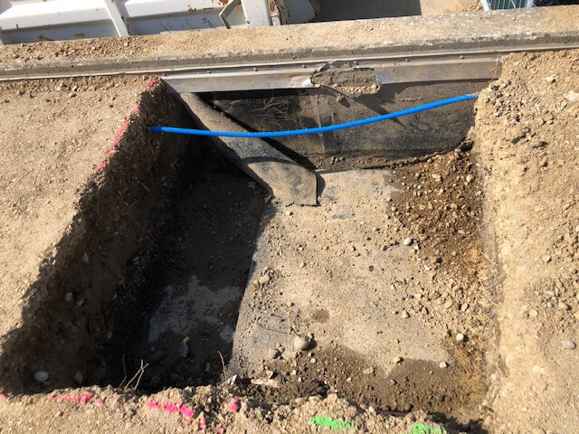 Une tranchée de câble mise à nu sur un chantier, on y voit du sable, de la terre et un câble bleu.