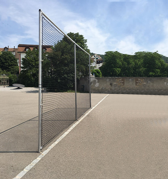 Ein Ballfangnetz auf einem freien, asphaltierten Sportplatz mit Bäumen und Häusern im Hintergrund