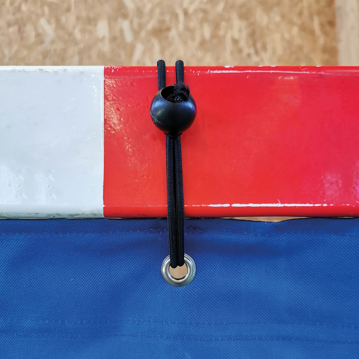 Nahaufnahme eines elastischen Spannseils mit schwarzem Kugelverschluss, befestigt an rotem und blauem Material mit Metallöse