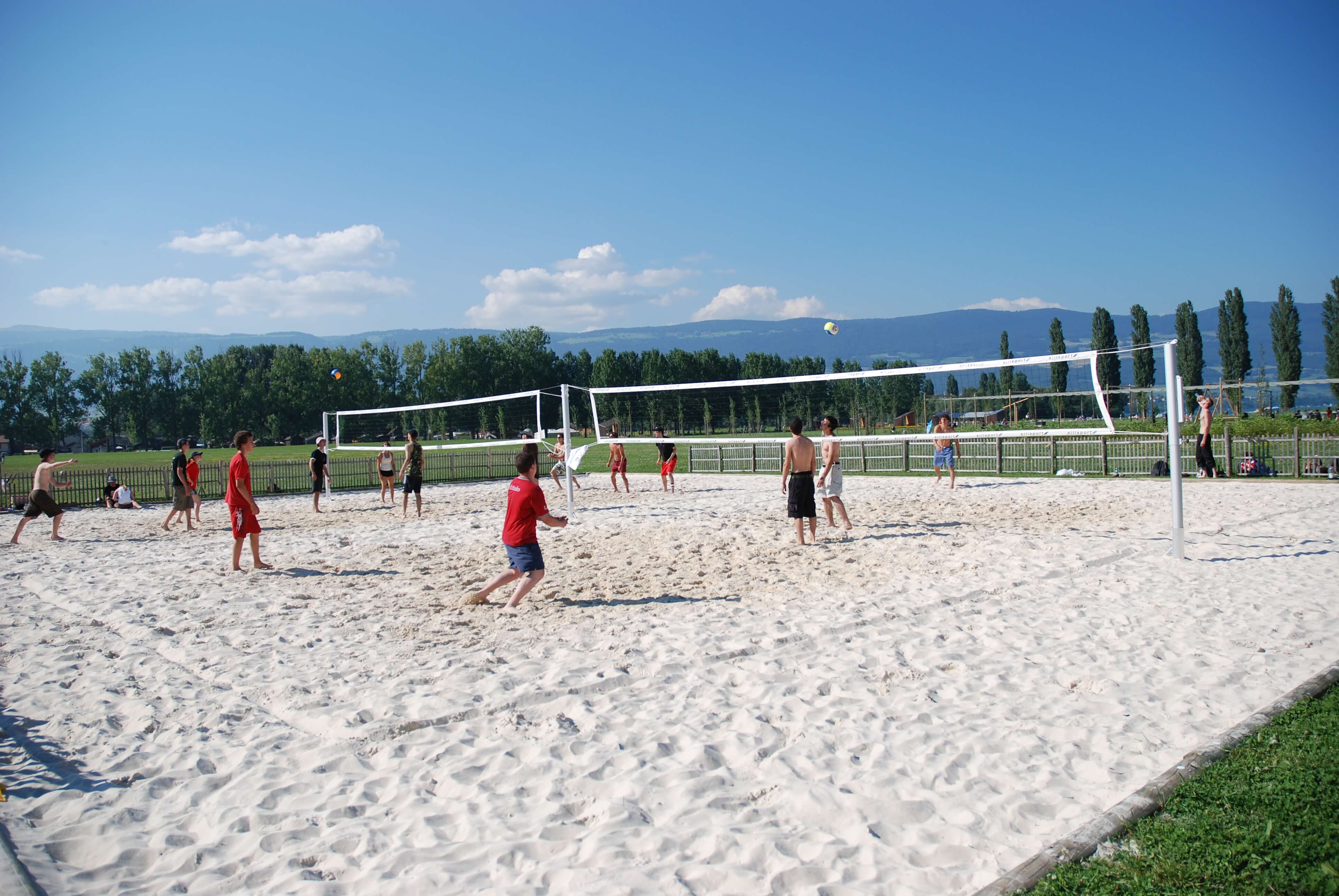 Gruppe von Jugendlichen beim Beachvolleyballspiel auf einem Sandplatz bei blauem Himmel