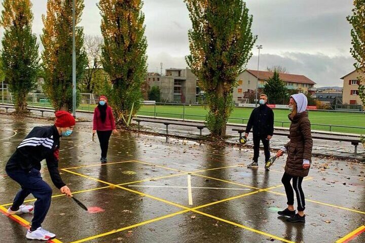 Des gens jouent au ping-pong sur un terrain de sport mouillé avec des arbres en arrière-plan