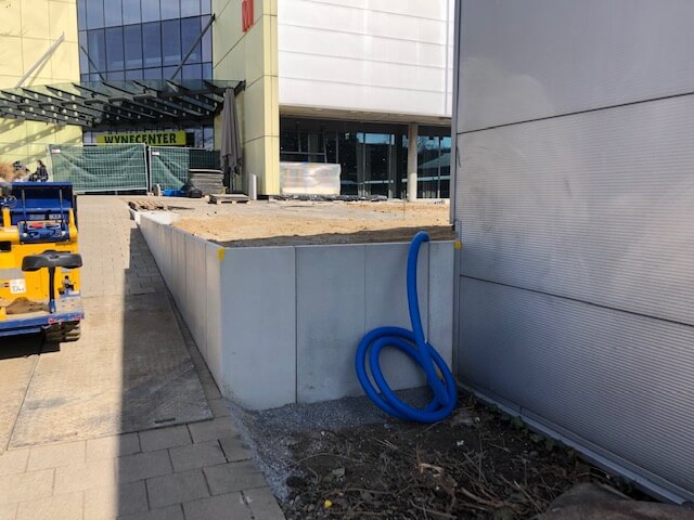 Eine Baustelle mit einer Rampe, Baucontainer und blauen Schläuchen vor einem Einkaufszentrum.