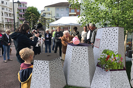Des personnes se rassemblent autour de mobilier urbain moderne dans un quartier résidentiel lors d'une fête citoyenne.