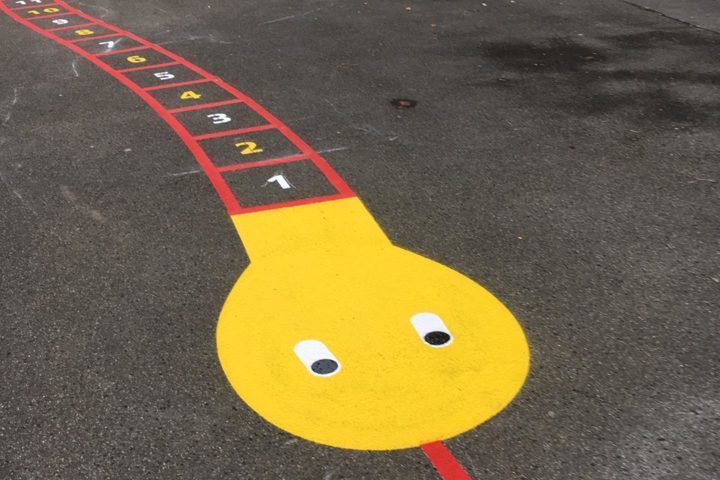 Serpent de jeu coloré avec des chiffres de 1 à 7 peints sur une aire de jeu en asphalte.