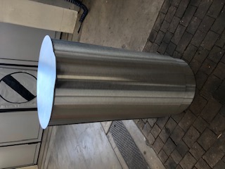 Une poubelle cylindrique en acier inoxydable est posée sur un sol en pierre dans une pièce à l'environnement industriel.